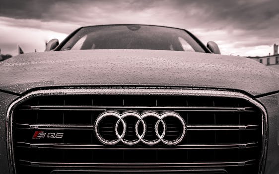 Close-up of a rain-covered Audi car grille showcasing luxury and elegance under cloudy skies.